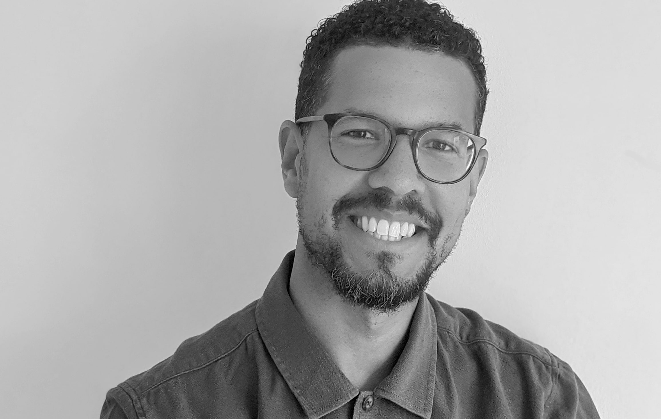 A black and white image of Rob Adediran. They are smiling towards the camera and wearing glasses.