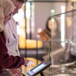 Two people using a digital touch screen together in a museum