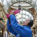 Experiencing Leeds 2023: A volunteer at Leeds 2023 takes a picture during a 'soundwalk' called As You Are, pointing their phone upwards to the ceiling in Leeds County Arcade.