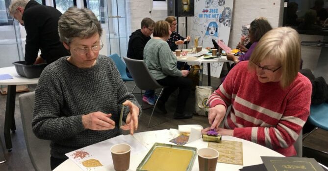 Two people taking part in a printing workshop. They are working at a circular table.