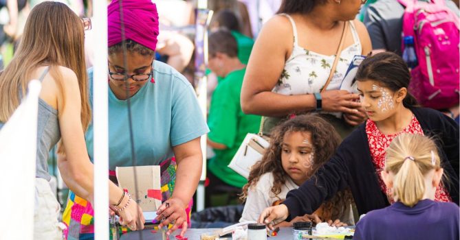Adults and children doing crafts together at an outdoor children's festival.