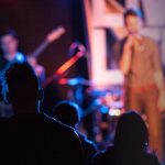 A crowd of young people watching a singer perform on stage.