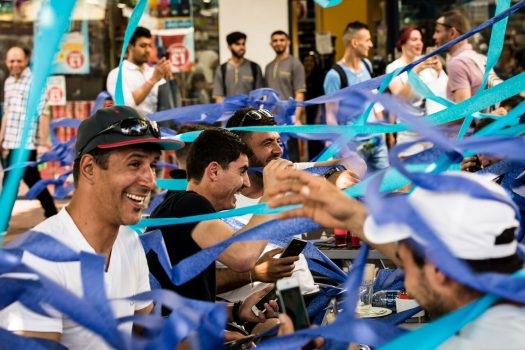 A group of men smiling and laughing surrounded by blue and purple streamers.