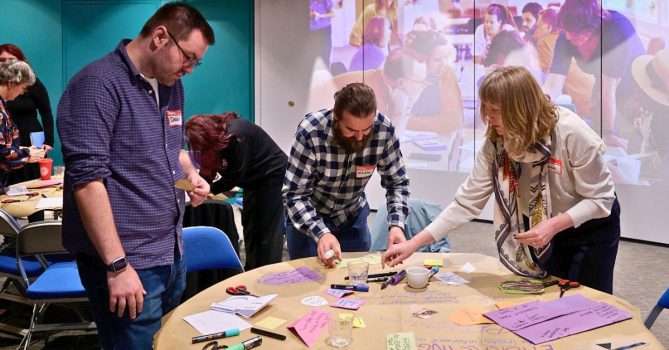 Three participants at a cultural vitality lab. They are stood around a table, making a collage together.